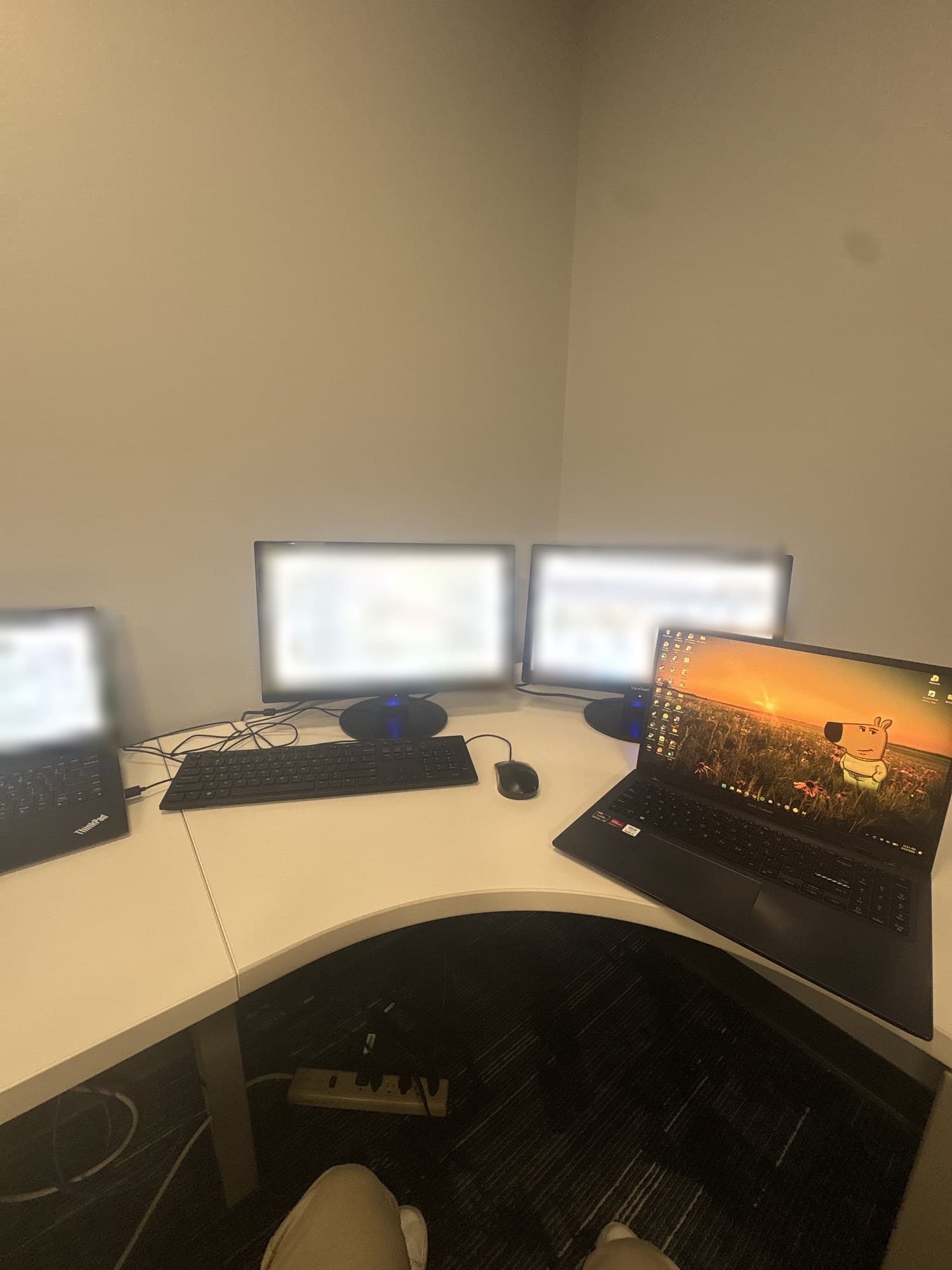 The same desk seen from standing height, the three work screens out of focus and a personal laptop open beside them.
